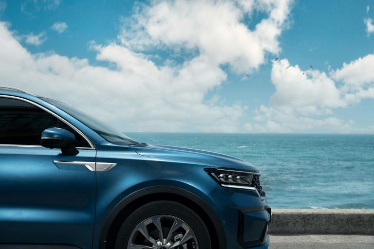 A stylish blue SUV parked by the ocean in Busan, South Korea, on a sunny day.